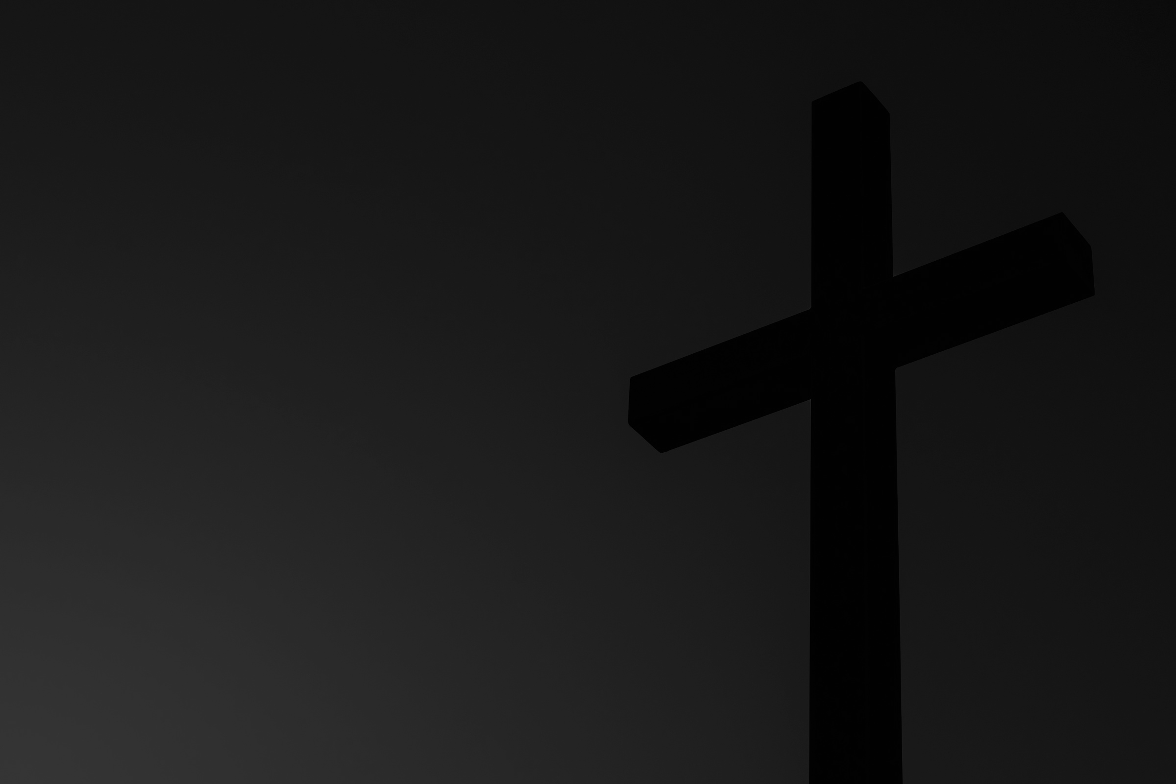 Sehr dunkles Schwarz-Weiß-Bild: Ein schwarzes Kreuz hebt sich vom grauen Hintergrund ab.